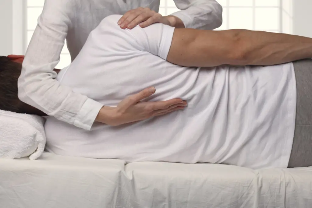 A chiropractor’s hands on the shoulder and low back of a patient lying on his side.