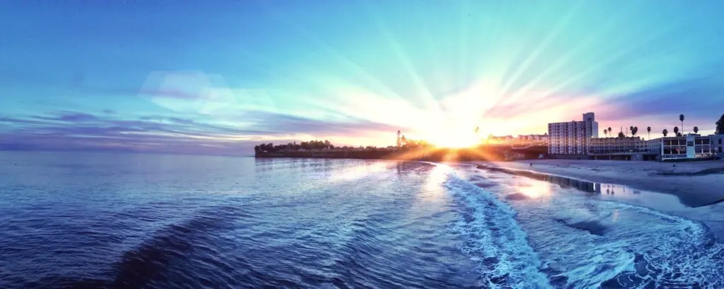 Sunrise over the water, light streaming across the waves toward a beachfront town.