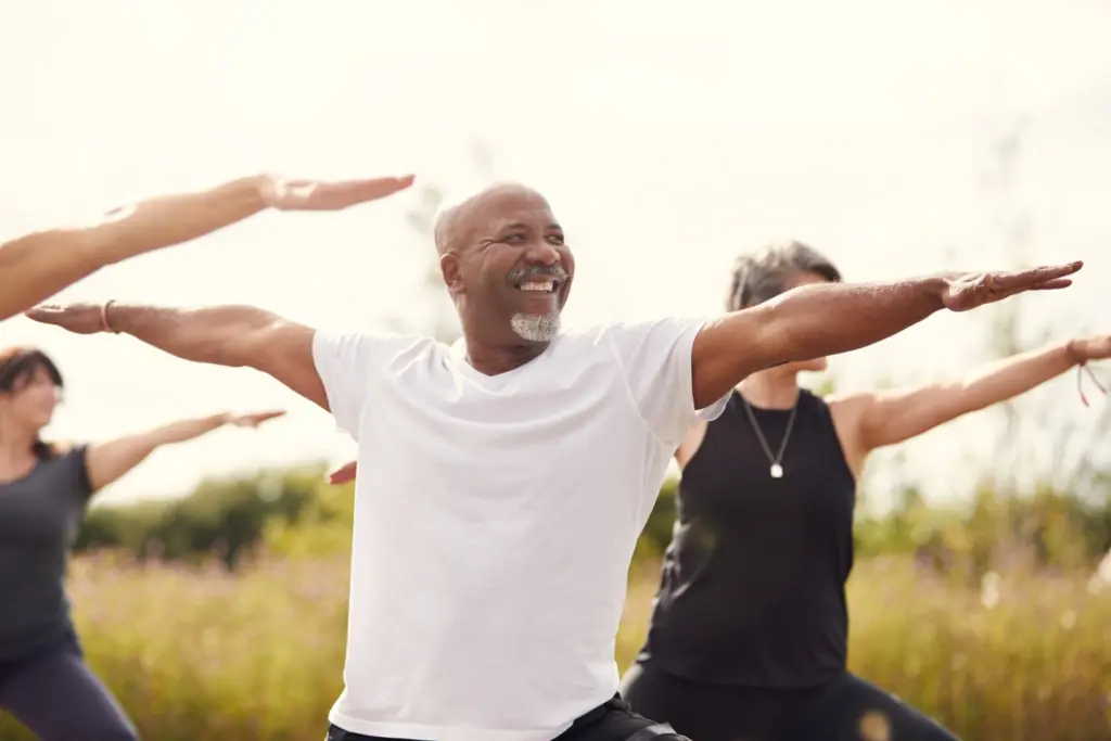 Older adults stretching their arms wide in a sunny meadow.