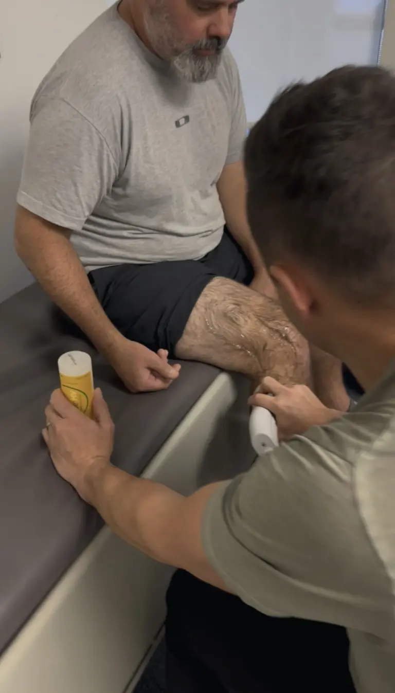 SoftWave therapy at Aptos Chiropractic: the applicator held to a seated patient’s knee.